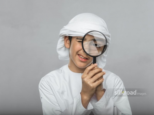 Middle Eastern boy looking through magnifier|