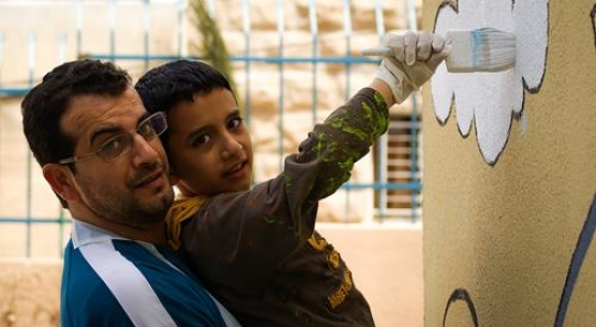 happy father and his son painting the wall of a kindergarten