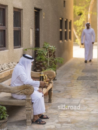 Arab grandfather sitting with his misbahah while a man is walking towards him|-