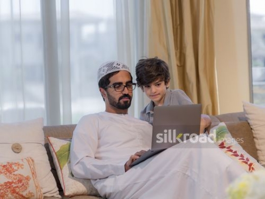 Young arab boy and arab man sitting together on the couch using the device|