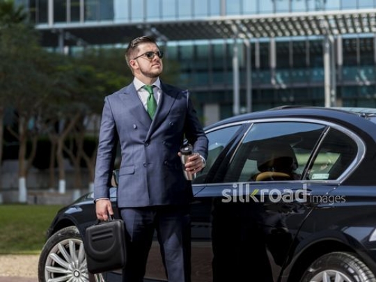 Western Businessman standing holding his laptop bag and a travel mug|-