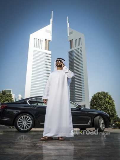 Middle Eastern man standing infront of his car using his mobile|-