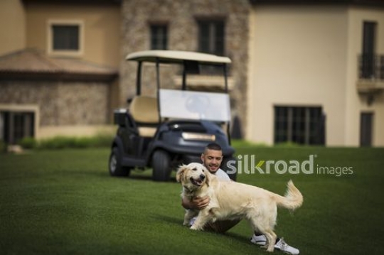 Arab man sitting on the grass playing with the dog|-