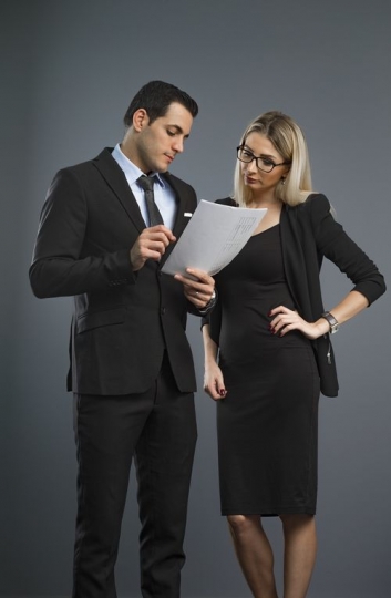Portrait of a business man and business woman standing talking about the paper in the man's hand|