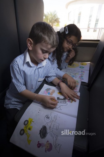 Kids sitting down together and colouring in their book |-