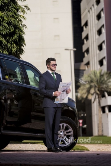 Businessman standing infront of his car with a newspaper |-