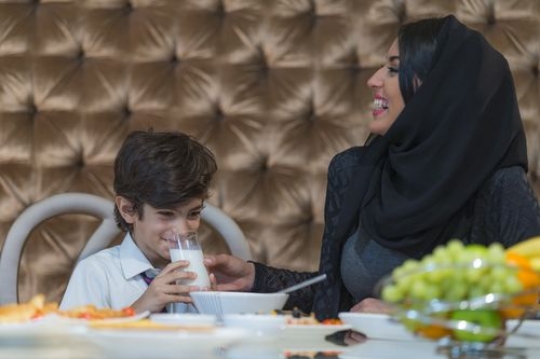 Arab mother sitting with her son while he is drinking milk|-