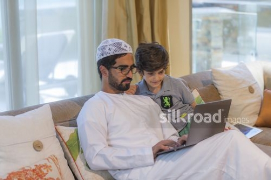Middle Eastern man using the laptop sitting with the young kid|
