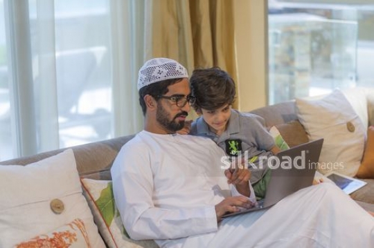Arab man sitting using the laptop with the young kid|