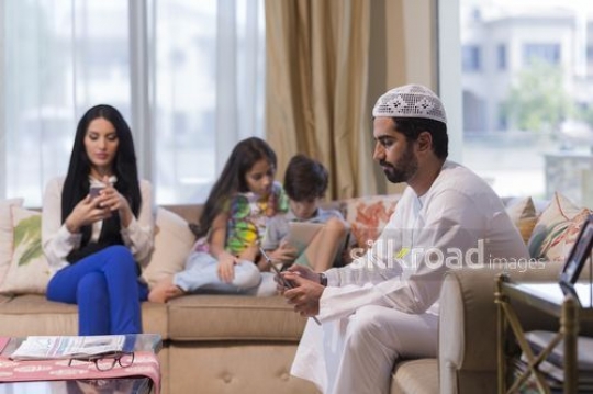Middle Eastern family sitting on the couch all on their devices|
