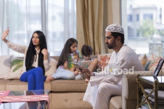 Arab woman taking a selfie sitting with the Middle Eastern man and young kids on the devices|