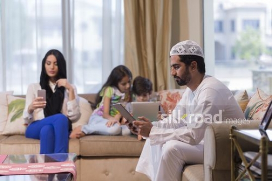 Arab family sitting together on the couch each one the device|