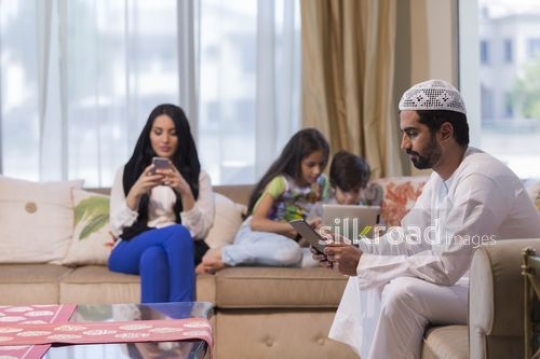 Middle Eastern family sitting together on the couch each one of their devices|