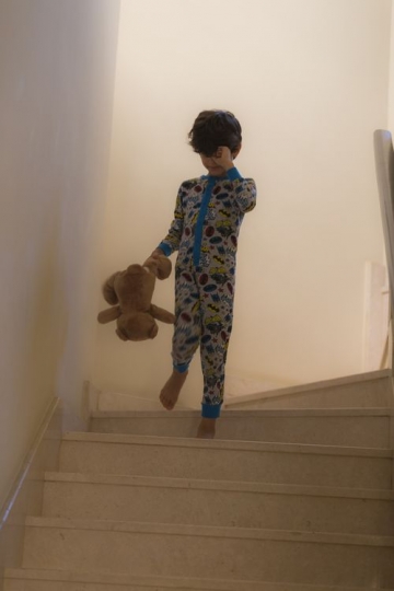 Middle eastern kid dressed in his pajamas walking down the stairs |-