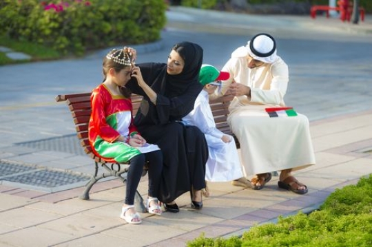 Middle eastern family sitting on the bench getting ready for national day|-