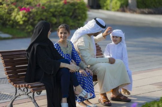 Middle eastern family sitting on the bench talking to each other|-