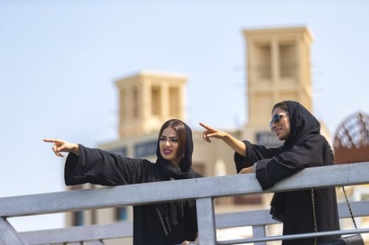 Women dressed in the traditional UAE attire standing by the dock talking to each other|