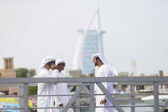 Arab man talking on the phone while standing with two of his friends by the dock|