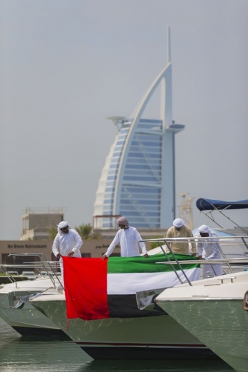 Men dressed in the traditional attire attaching the UAE flag to the yacht to celebrate National Day|