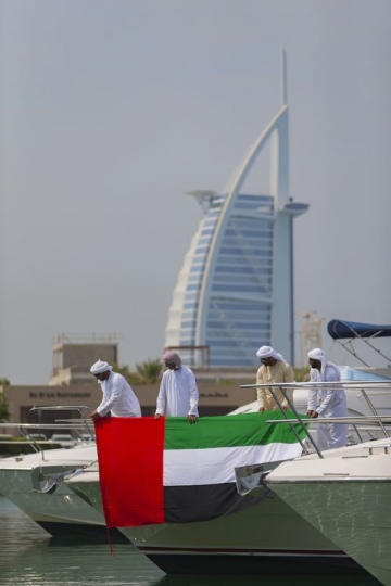 Arab men standing by the yacht holding a UAE flag|