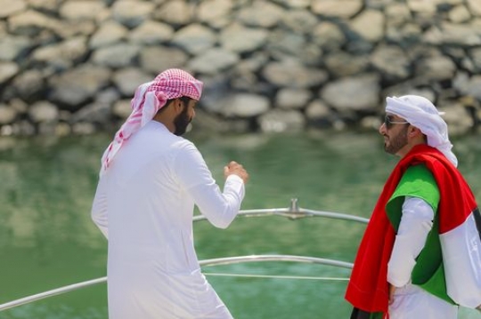 Arab man standing on the deck of the yacht while one man is carrying the UAE Flag on his shoulder|