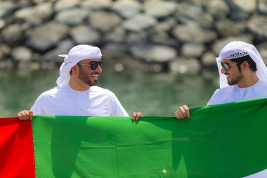 Medium shot of two arab men celebrating National Day while holding a UAE Flag|