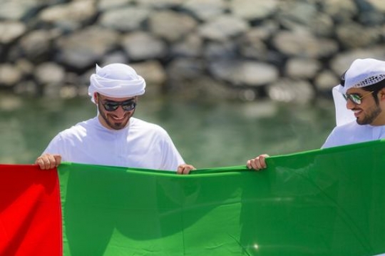 Two arab men holding a UAE flag for the celebrations of National Day|