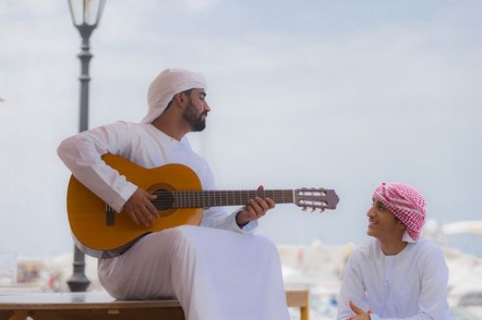 Arabian man sitting with his friend and playing an instrument |