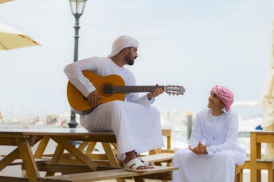 Arab man playing the instrument while sitting with his friend|