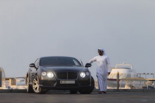 Arab man dressed in the traditional attire closing the door of the luxury car|-