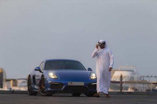 Arab man dressed in traditional attire wearing his sunglasses while walking away from his vehicle|-