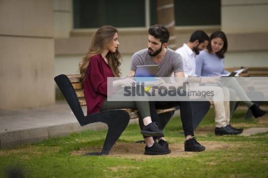 Middle Eastern students sitting on the bench talking|