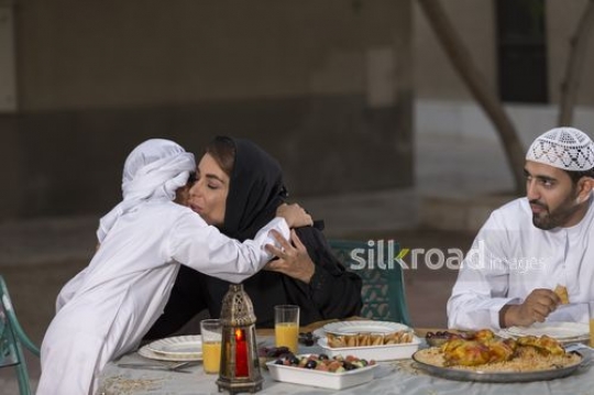 REPLACE - Arab mother hugging her son at the dinning table |-