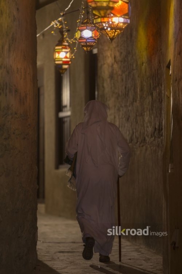 Middle Eastern man strolling through alley decorated by Ramadan lanterns|-
