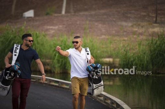 Young Middle Eastern men carrying Golf bags walking together|-