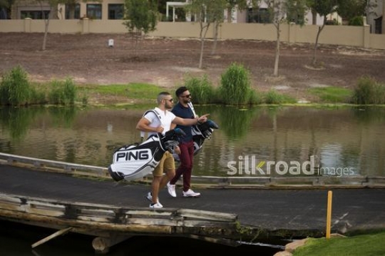 Young arab men walking together carrying golf bags|-
