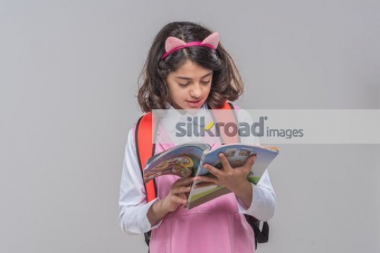 Middle Eastern girl reading the book carrying her school bag|