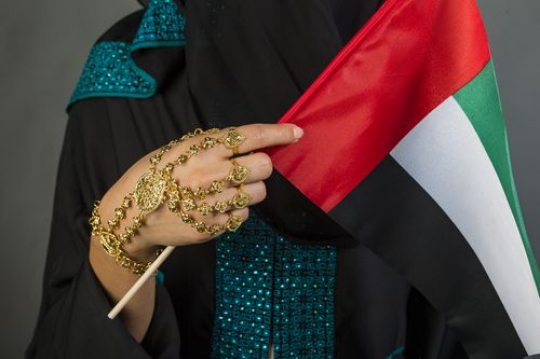 Close up of a woman wearing her traditional jewellery  with the UAE flag in her hand